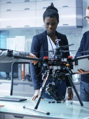 Multi Ethnic Team of Young Female and Male Engineers Working on Modern Drone Prototype. They're in a Bright High-Tech Laboratory.
